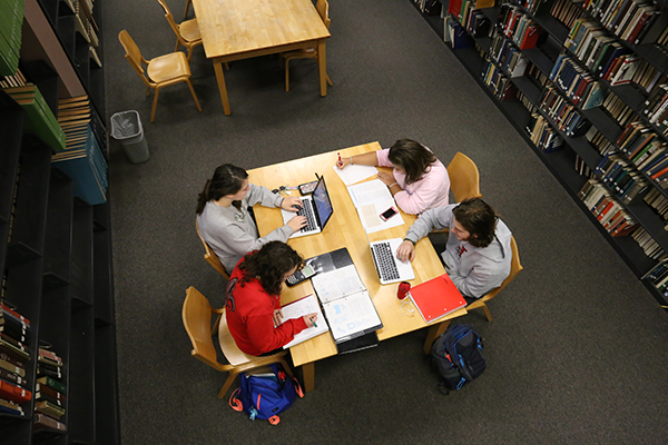 Four students sit and study at a desk in the library 