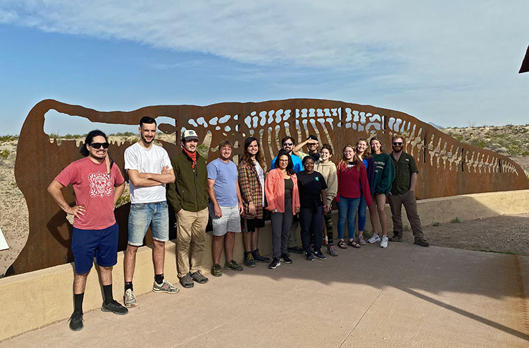 University of Louisiana at Lafayette paleontology majors in front of a large metal cutout of a crocodile skeleton