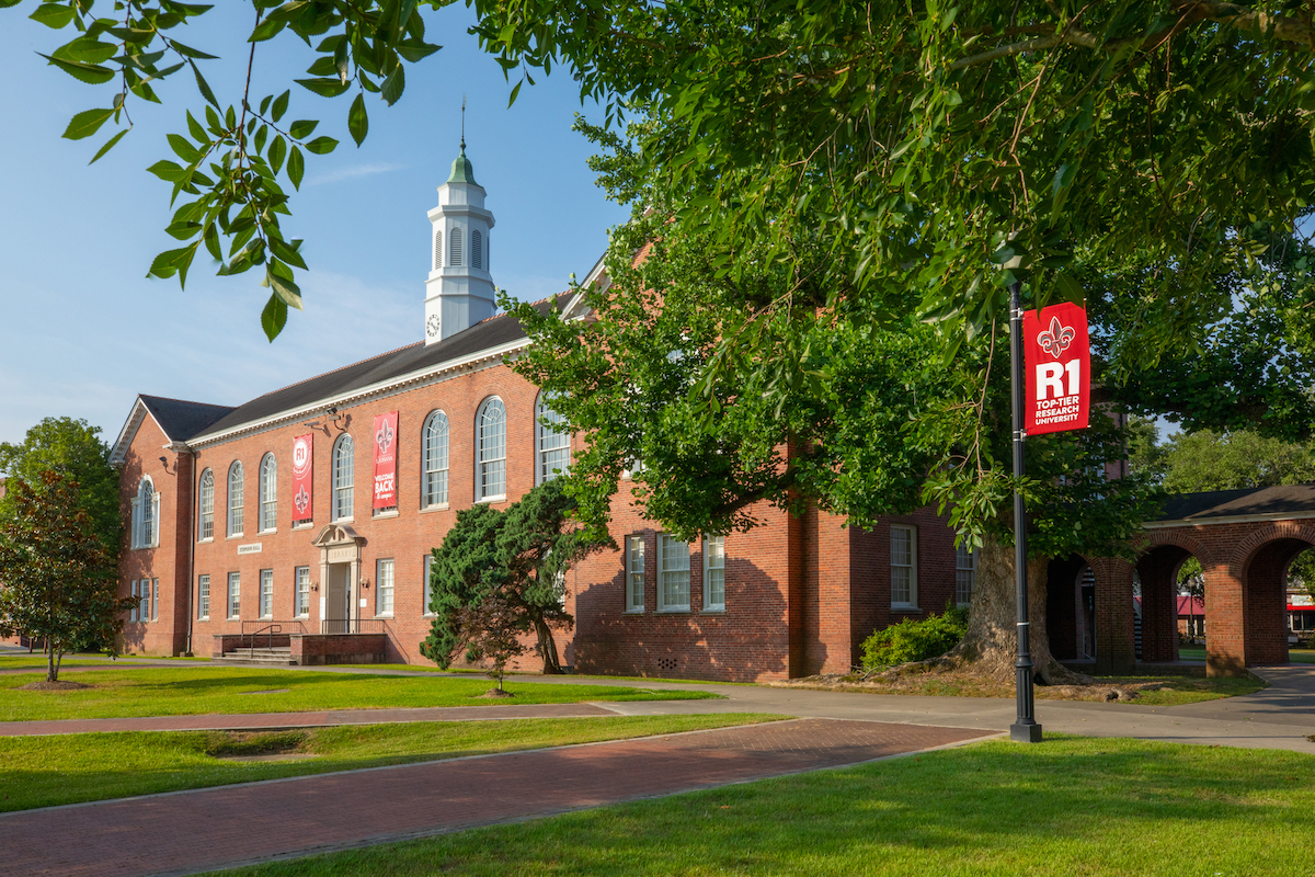 Stephens Hall from the UL Lafayette Quad with R1 flags hanging on the building and flag pole