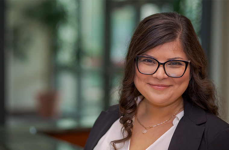 Lizzette Phillips, MBA graduate, pictured inside her office building wearing a dark blazer and glasses.