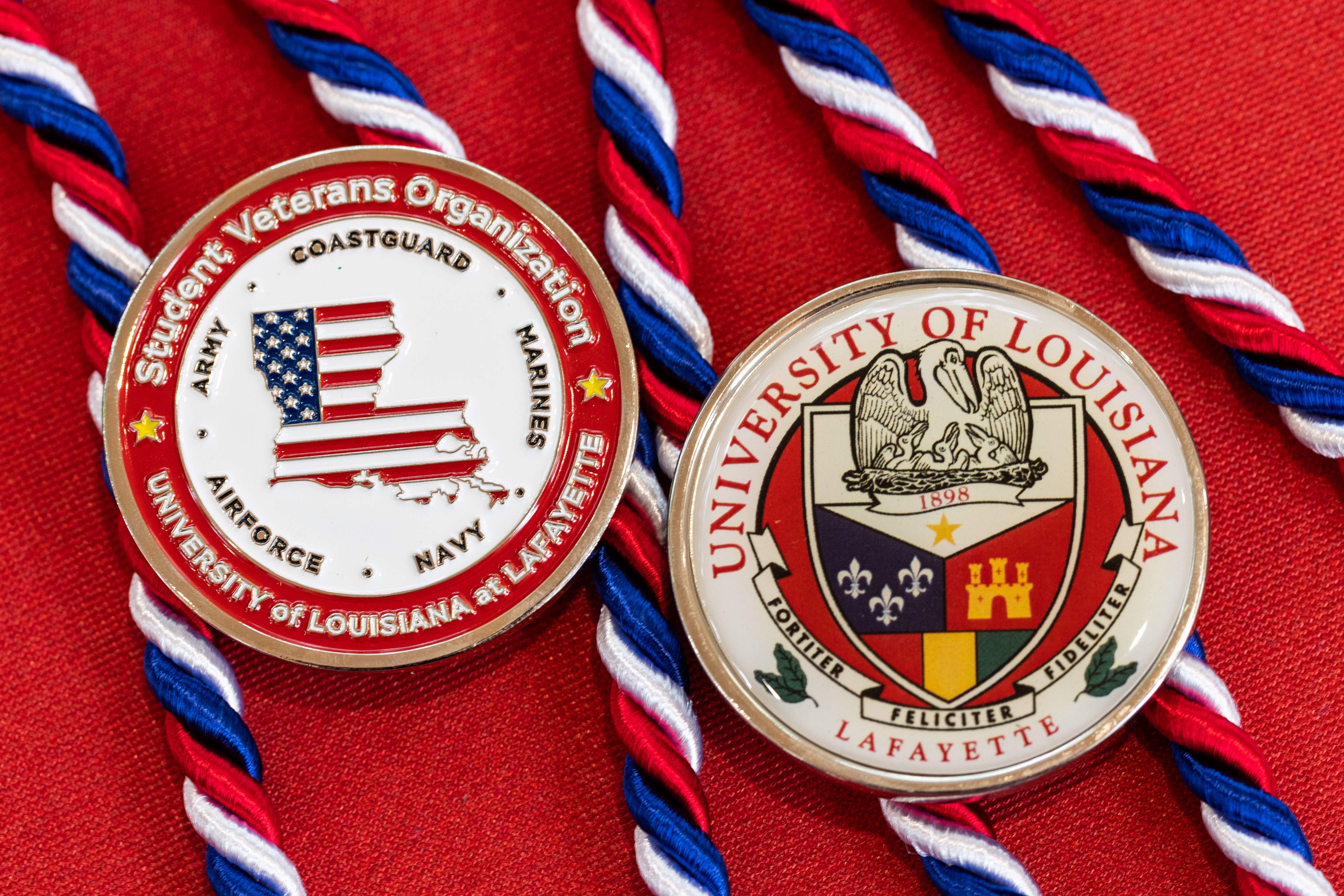 Two University of Louisiana at Lafayette medals on red background, left medal of the Student Veterans Organization, right medal of University crest
