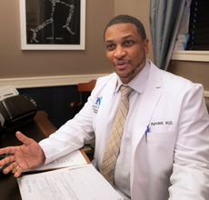 MBA in Health Care Admin graduate discusses paperwork, wearing his white surgeon coat. 