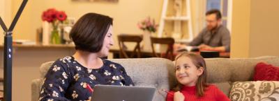 UL Lafayette online student working at a computer on the couch next to their child with their spouse in the background.
