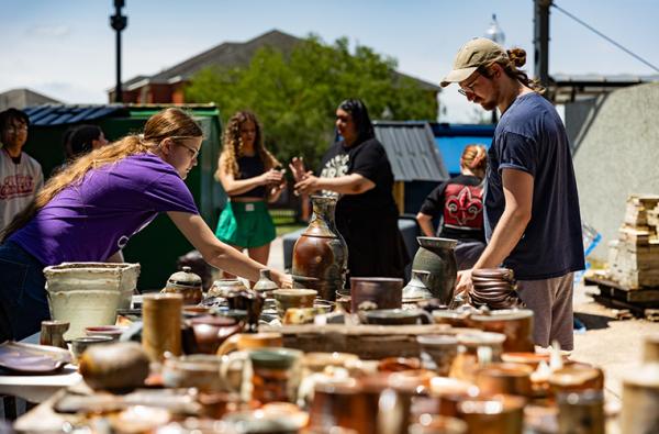 UL Lafayette students and community members surrounding tables covered in student ceramic works for sale.