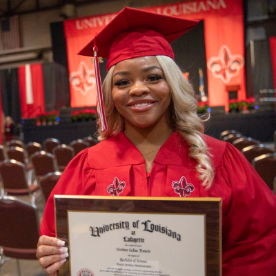 Destinee Francis smiles for a portrait at Commencement. She is wearing her UL Lafayette cap and gown and holding up her B.S. in Health Services Administration diploma.