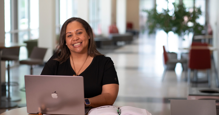 Graduate of the RN to BSN online program works on laptop while wearing black scrubs.
