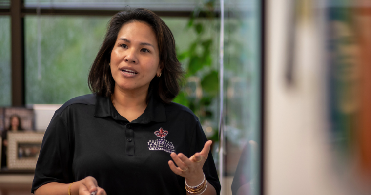 Graduate of the online mba program speaks at a white board, wearing a black UL Lafayette MBA Association polo.