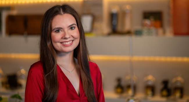 Graduate of UL Lafayette's psychology degree program smiles in front of a store display, wearing a red blouse.
